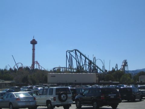 1990 Ford Bronco - tall observation tower and dark roller coaster tracks rise behind a parking lot packed with parked cars and SUVs.
