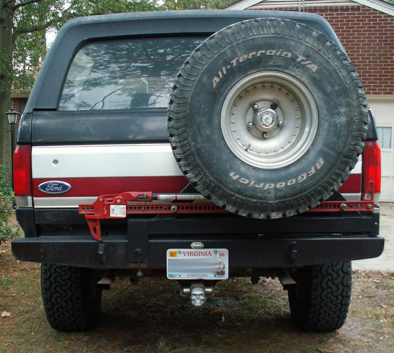 Rear view of a dark blue and red 1987 Ford Bronco with a spare tire mounted on the tailgate and a black bumper