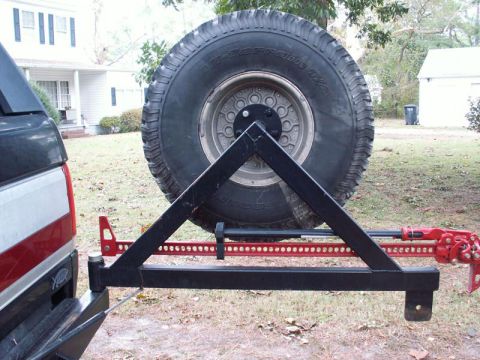 1988 Ford Bronco - A black metal spare tire carrier with a hi-lift jack is mounted on the rear of a red and white truck.