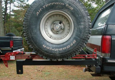 1988 Ford Bronco - Spare tire and Hi-Lift jack mounted on the rear of a 1988 Ford Bronco, with another vehicle visible to the left.