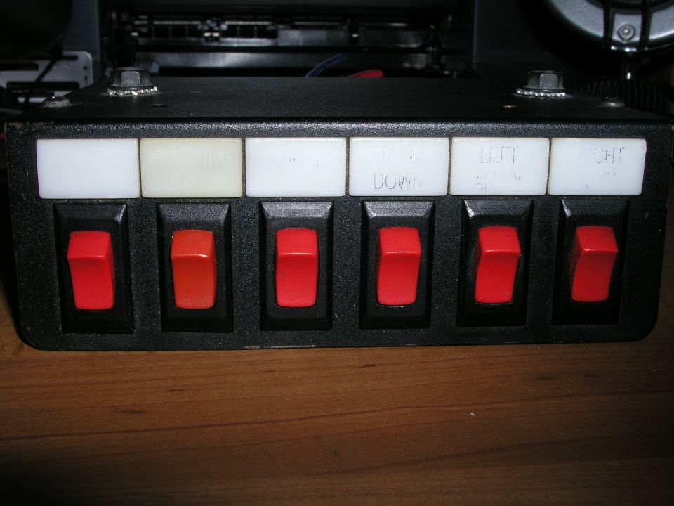 Black switch panel with six red rocker switches and white labels above them. Some labels read 'DOWN', 'LEFT', and 'RIGHT'