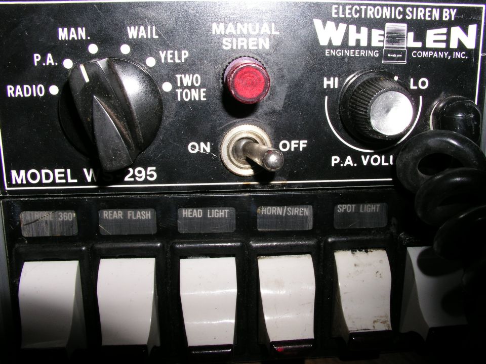 Whelen V295 siren control panel with knobs for MAN, WAIL, YELP, TWO TONE, P.A., RADIO, HI, LO, and P.A. VOLI. Includes ON/OFF toggle and switches for 360, REAR FLASH, HEAD LIGHT, HORN/SIREN, SPOT LIGHT