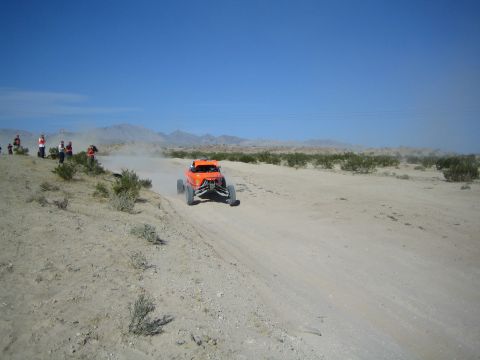 Orange off-road buggy racing toward camera on a dusty desert trail