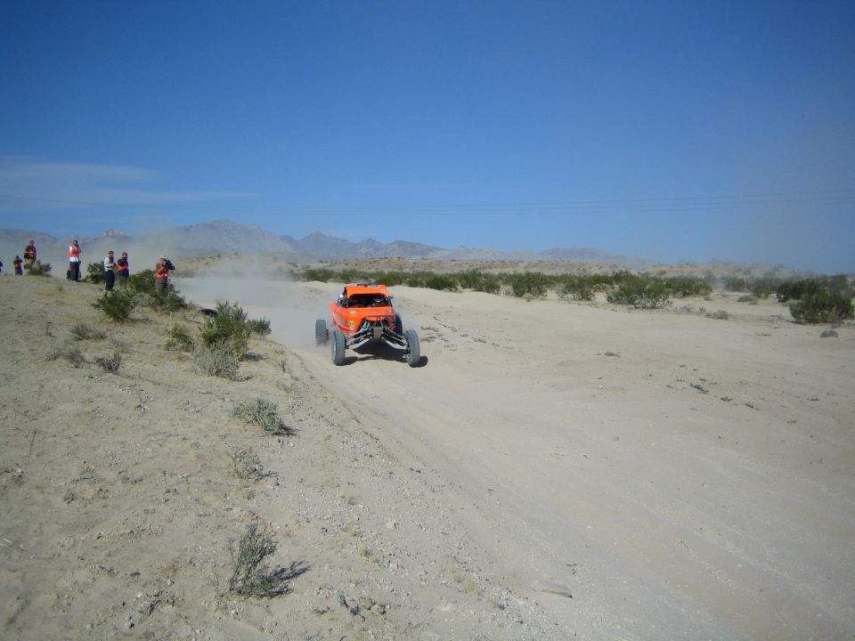Orange off-road buggy racing toward camera on a dusty desert trail