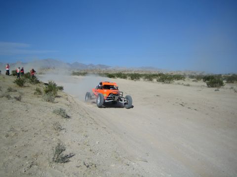 Orange off-road race buggy cornering through desert sand with a dust trail