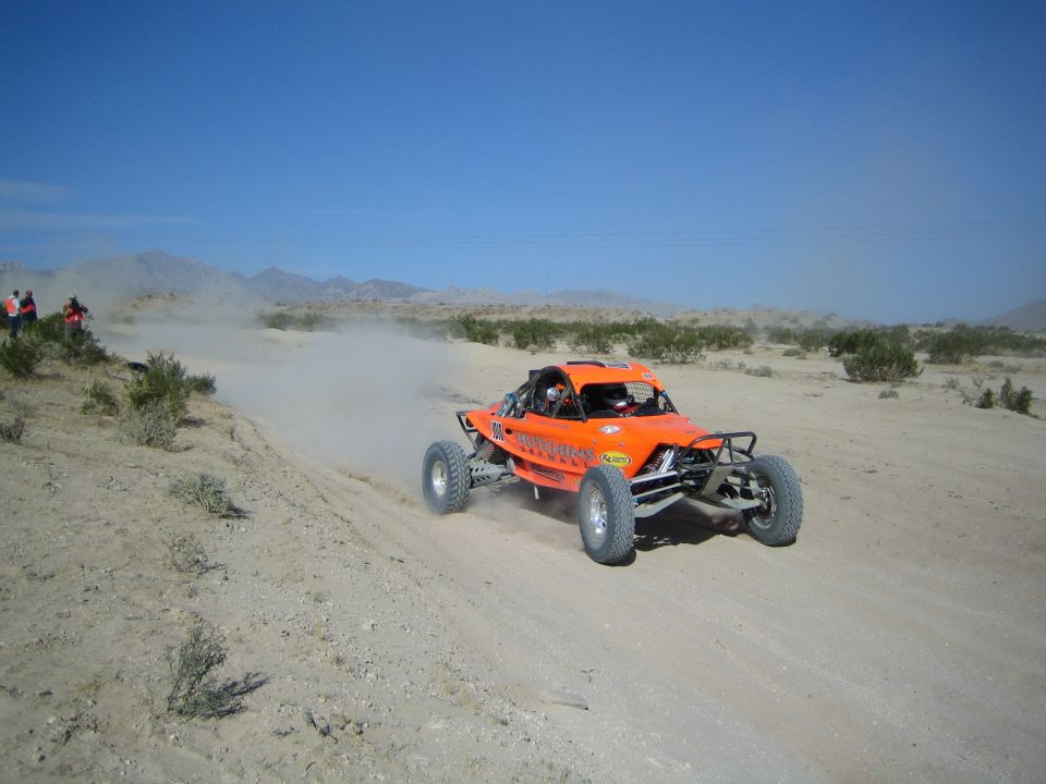 Orange tube-frame off-road race buggy speeding across open desert terrain