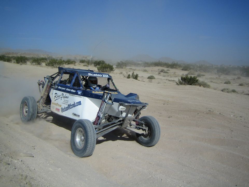 Blue and white off-road race buggy racing across the desert with sponsor decals