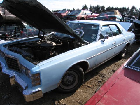1991 Ford LTD Crown Victoria - light blue full-size four-door sedan with its hood raised, parked among other vehicles in a junkyard setting.