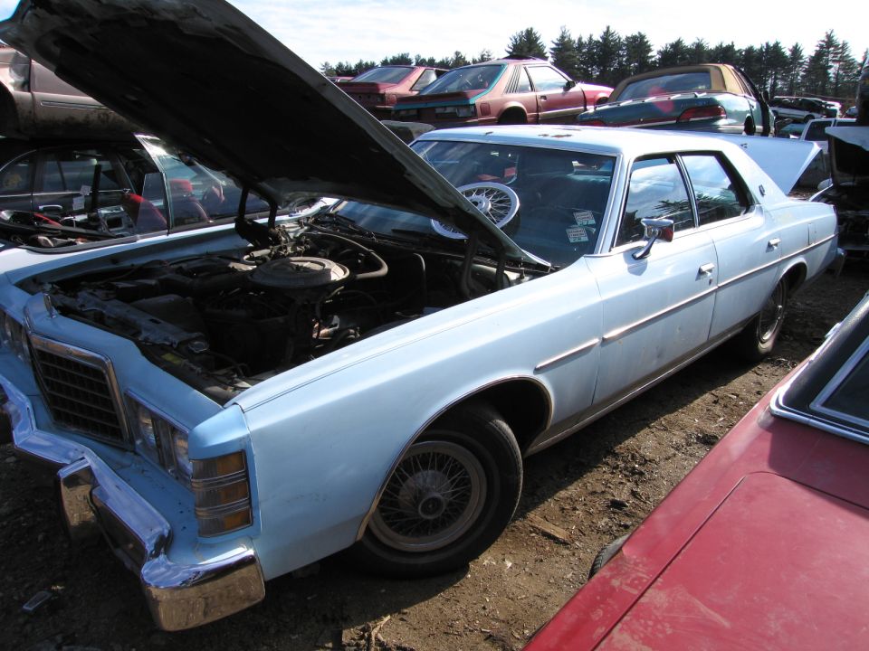 Light blue full-size sedan with hood open in a salvage yard