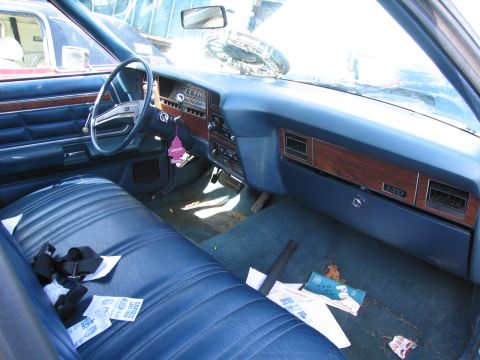 1991 Ford LTD Crown Victoria - Faded blue car interior showing a bench seat, woodgrain dashboard trim, and scattered papers on the floor.