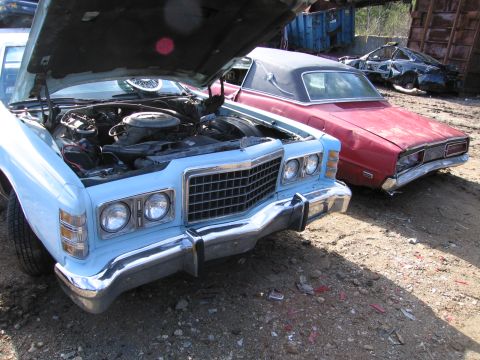 1991 Ford LTD Crown Victoria - Light blue sedan with hood up exposing the engine, next to a maroon convertible in a salvage yard.