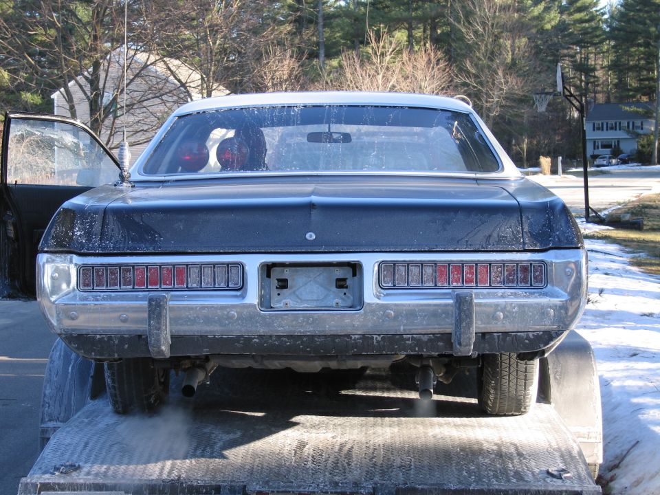 Rear of a dirty dark coupe on a trailer with dual taillights