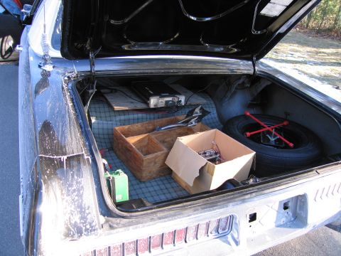 1991 Ford LTD Crown Victoria - open trunk of a sedan reveals a spare tire, a wooden tray, a cardboard box and assorted tools on a plaid trunk liner.