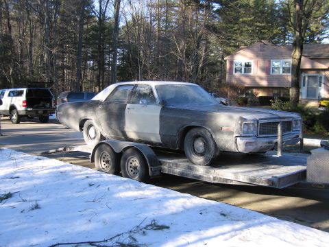 1991 Ford LTD Crown Victoria - Front three-quarter view of a grimy dark full-size sedan with a chrome grille on a tandem-axle car trailer in a snowy driveway.