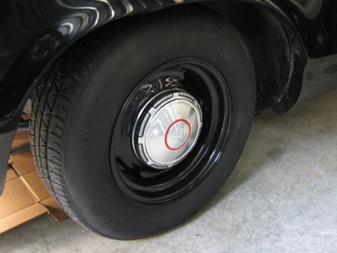 1991 Ford LTD Crown Victoria - Close-up of a black-painted steel wheel fitted with a chrome dog-dish hubcap with a red accent ring on a blackwall tire.