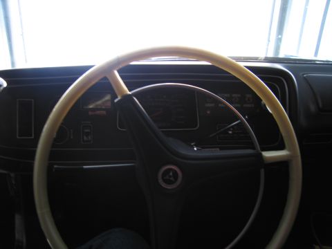 1991 Ford LTD Crown Victoria - cream-colored two-spoke steering wheel with a Pentastar horn button sits before a dark instrument panel with backlit gauges.