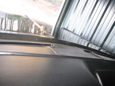 1991 Ford LTD Crown Victoria - View across the top of a dark vinyl dashboard and windshield with wipers, looking out toward a corrugated metal building and trees.