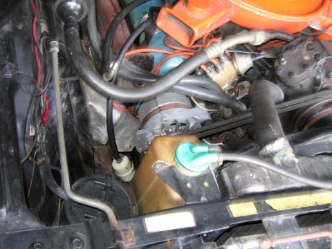 1991 Ford LTD Crown Victoria - detailed engine bay view with an orange air cleaner above, looping rubber hoses and a brass-colored bracket beside a teal-capped fitting.