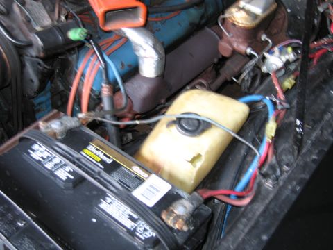 1991 Ford LTD Crown Victoria - engine bay showing a blue valve cover, orange and blue wiring, a black battery and a yellowed plastic fluid reservoir.