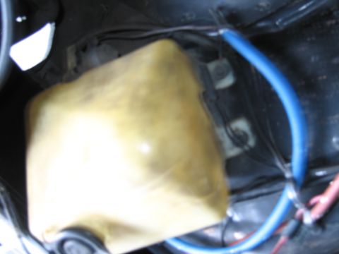 1991 Ford LTD Crown Victoria - close view of a yellowed translucent plastic fluid reservoir sitting in a black engine bay with blue and red wires running past it.
