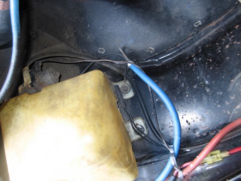 1991 Ford LTD Crown Victoria - engine bay corner showing blue and red wires with a fuse connector routed around a yellowed plastic reservoir on black sheet metal.