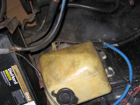 1991 Ford LTD Crown Victoria - yellowed plastic fluid reservoir sits above a black DieHard Gold battery in an engine bay, with blue and red wires running nearby.