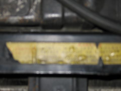 1991 Ford LTD Crown Victoria - weathered translucent-yellow fluid reservoir mounted between metal engine parts, with a dark hose running alongside.