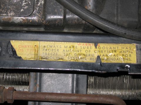 1991 Ford LTD Crown Victoria - aged Chrysler cooling-system warning label affixed near a radiator, instructing to maintain proper antifreeze coolant levels.