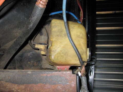 1991 Ford LTD Crown Victoria - aged off-white plastic washer-fluid reservoir mounted in an engine bay beside rusty metal and colored wiring.