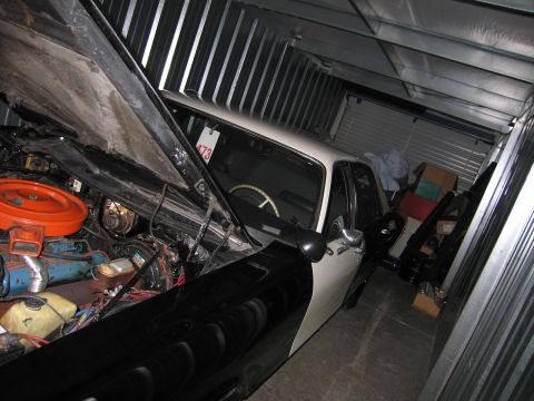 1991 Ford LTD Crown Victoria - two-tone car parked inside a metal storage unit with its hood up, exposing an engine topped by an orange air cleaner.