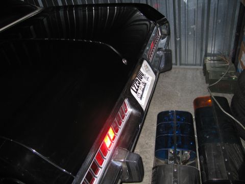 1991 Ford LTD Crown Victoria - rear corner of a black car with an illuminated taillight, parked beside blue and amber rotating emergency beacon lights.
