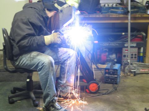 1995 Ford Bronco - A person is welding in a garage, sparks flying from the metal being worked on.