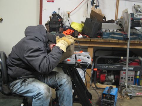 1995 Ford Bronco - A person is welding in a cluttered workshop with various tools and machinery around them.