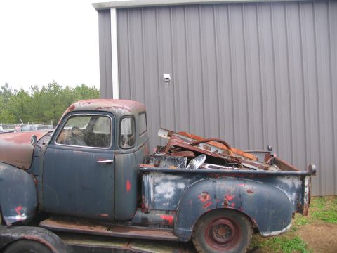 1949 Chevrolet C/K Pickup - A weathered pickup truck, likely from the late 1940s, sits loaded with debris beside a corrugated metal structure.