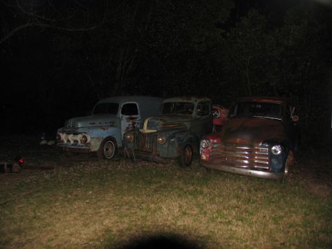 1949 Chevrolet C/K Pickup - Three vintage pickup trucks are lined up outdoors at night, showing significant rust and wear.