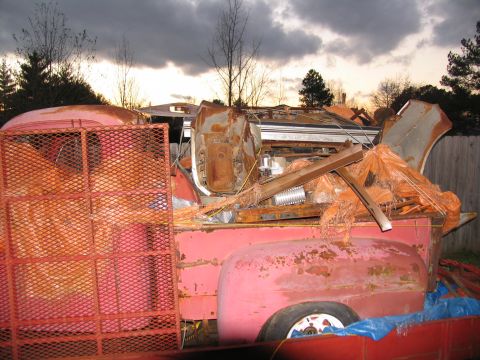 1952 Ford Pickup - A heavily rusted red pickup truck bed is loaded with debris under a cloudy sky.