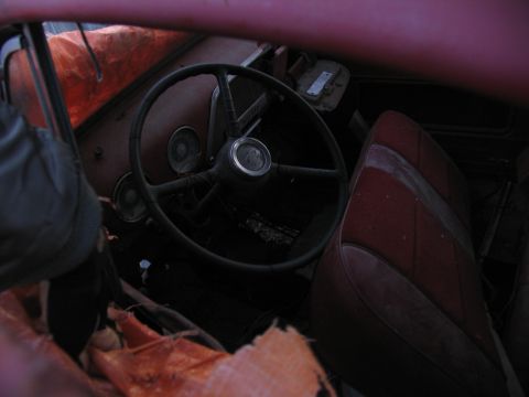 1952 Ford Pickup - Interior view of a car with worn red seats and a large steering wheel.