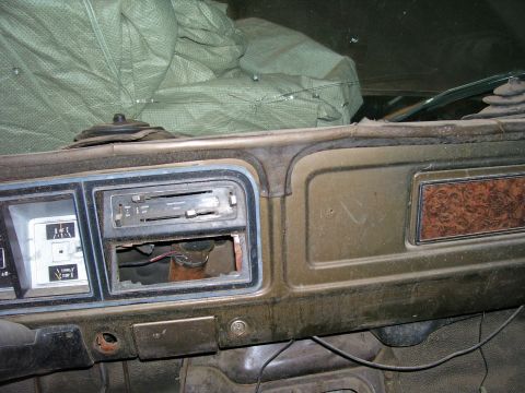 1979 Ford Bronco - The interior of an older vehicle shows a dusty dashboard with a radio delete and wood-grain accent panel.