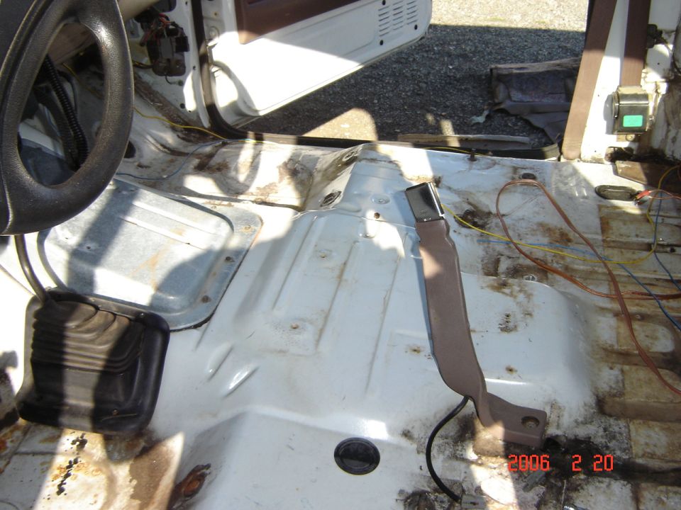 Stripped truck interior showing bare white floor pan, pedal boot, loose wiring and seat belt trim