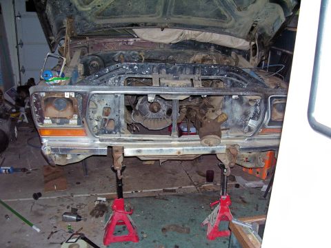 1979 Ford Bronco - The front end of a 1979 Ford Bronco is shown disassembled and supported by jack stands, revealing the engine and chassis components.