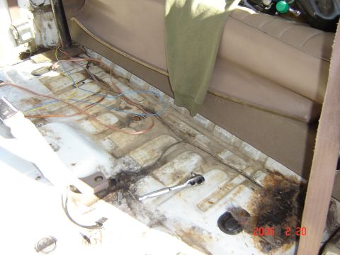 1993 Ford Bronco - The interior floor of a vehicle shows exposed wiring, rust, and a socket wrench, indicating a state of disrepair or ongoing work.