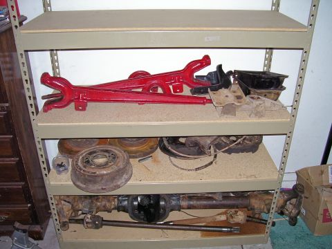 1979 Ford Bronco - Shelving unit filled with assorted automotive parts, including axles and brake drums.