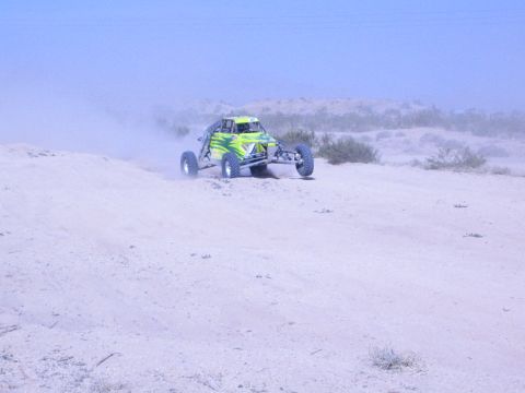 Green and silver off-road buggy cresting a sandy desert rise in hazy light