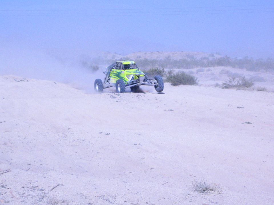 Green and silver off-road buggy cresting a sandy desert rise in hazy light