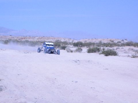 Blue and white off-road buggy on a distant desert track with mountains behind