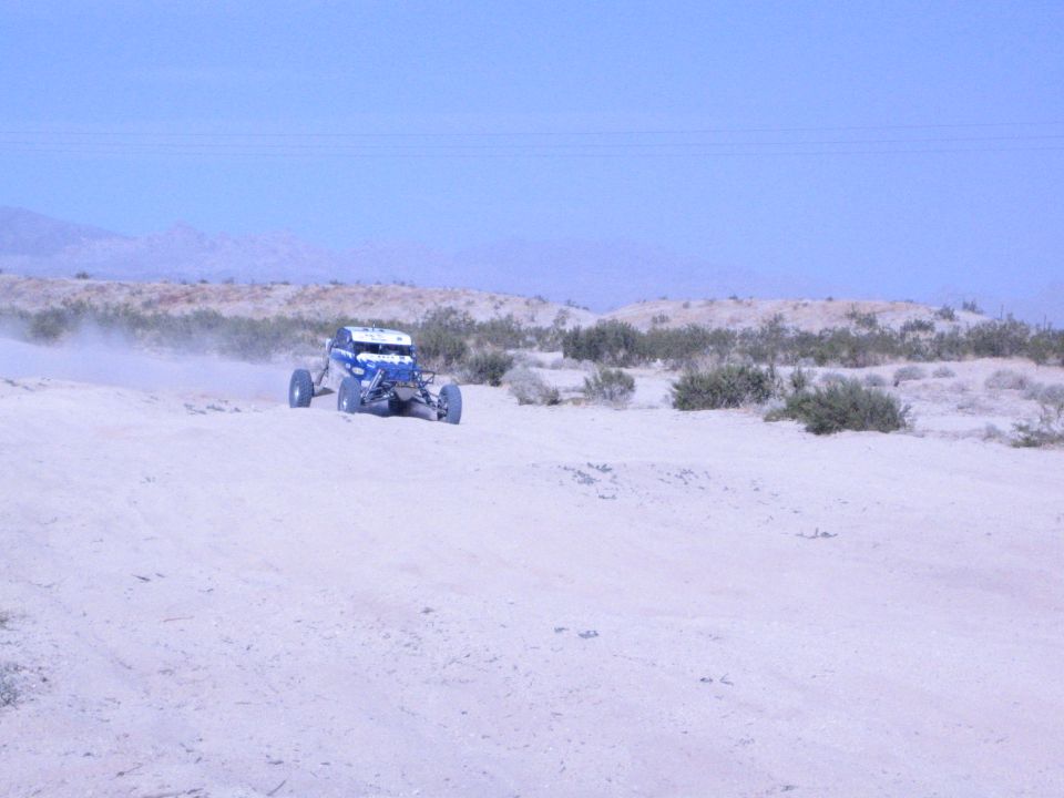 Blue and white off-road buggy on a distant desert track with mountains behind