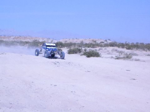 Blue and white off-road race buggy crossing open desert sand kicking up dust