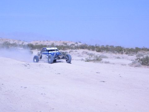 Blue and white off-road buggy speeding along a sandy desert ridge