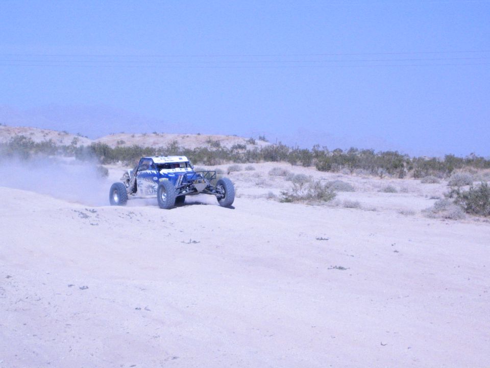 Blue and white off-road buggy speeding along a sandy desert ridge