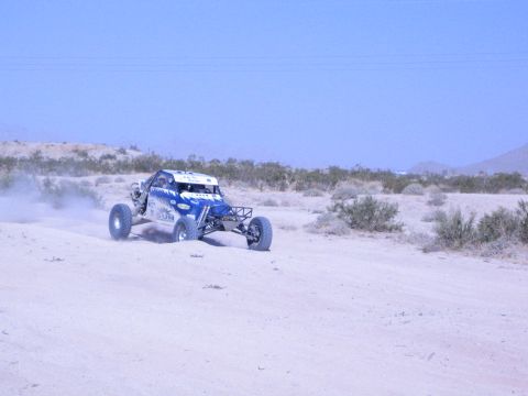 Blue and white off-road race buggy cornering on a dusty desert course